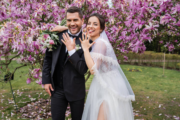 Веселая невеста торчит язык возле жениха показывая кольцо в парке 