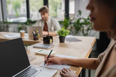 blurred interracial colleagues working with laptops in modern office