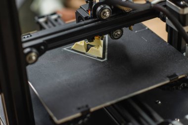 close up view of 3D printer creating plastic model near blurred figures and laptop in office