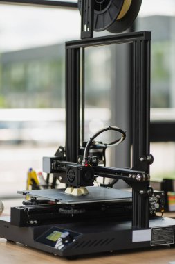3D printer creating plastic model on table near window in modern office