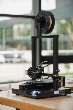 3D printer creating plastic model near produced figure on table in modern office