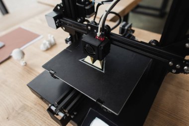 high angle view of 3D printer creating plastic model on table near blurred figures in office