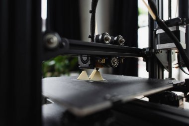 close up view of 3D printer creating plastic model near produced figure on table in modern office