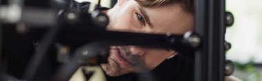 close up view of concentrated young designer looking at 3D printer in modern office, banner