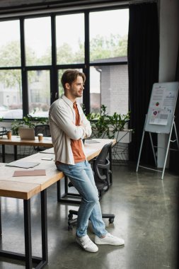 thoughtful young man in casual clothes with crossed arms standing in modern open space