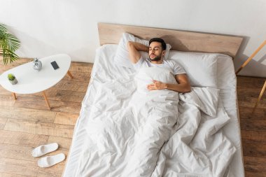 Akıllı telefon ve çalar saatin yanındaki beyaz yatakta uyuyan sakallı adamın en iyi görüntüsü.