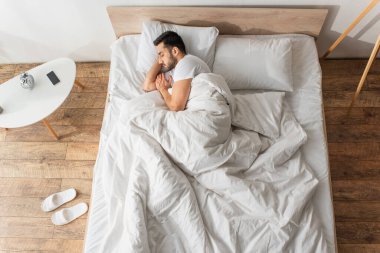 Side view of young man sleeping near cellphone and sleepers at home  clipart