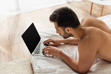 Yatakta boş ekranlı dizüstü bilgisayar kullanan üstsüz tele-işçiyi yüksek açılı görmek 