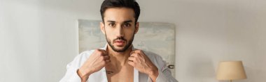 Genç adam gömlek ve afiş giyerken kameraya bakıyor. 