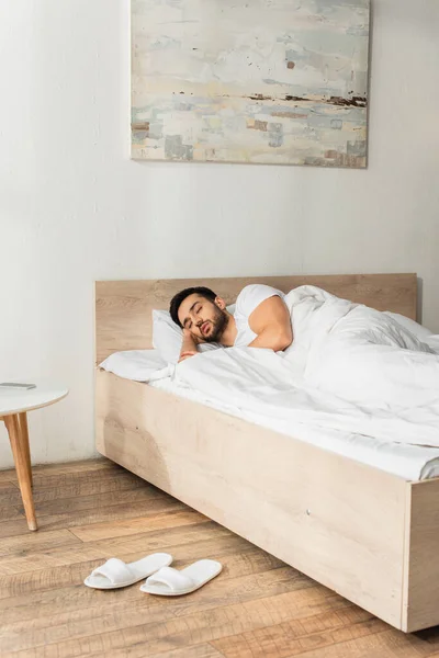 Bearded man sleeping near slippers and smartphone in bedroom