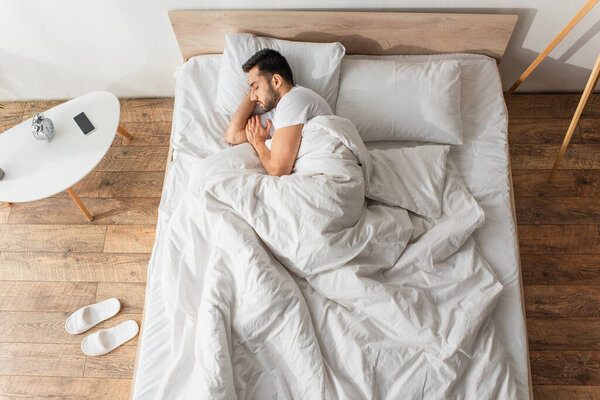 Side view of young man sleeping near cellphone and sleepers at home 