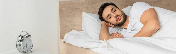 Νεαρός Άνδρας Κοιμάται Κοντά Ξυπνητήρι Στην Κρεβατοκάμαρα Πανό — Φωτογραφία Αρχείου