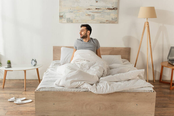 Side view of man sitting on bed at home 