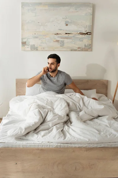 Bärtiger Mann Sitzt Auf Bett Und Telefoniert Mit Smartphone — Stockfoto