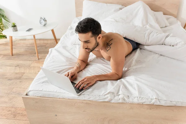 早上在床上使用手提电脑的纹身男子的头像 — 图库照片