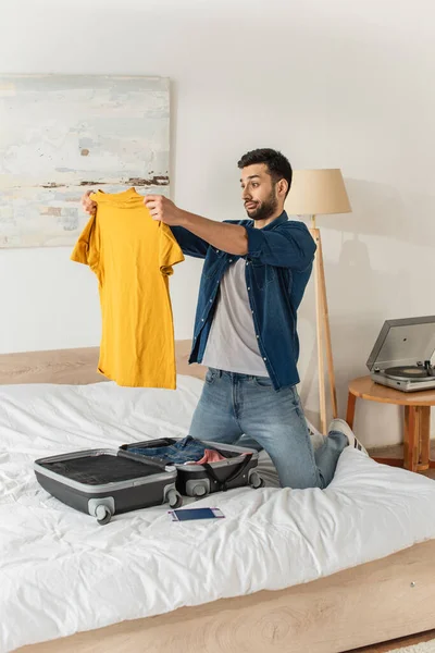 Aggressiver Mann Sieht Shirt Neben Koffer Und Reisepass Schlafzimmer — Stockfoto
