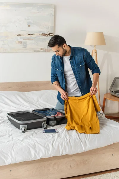 Jovem Segurando Camiseta Olhando Para Mala Perto Passaporte Cama — Fotografia de Stock