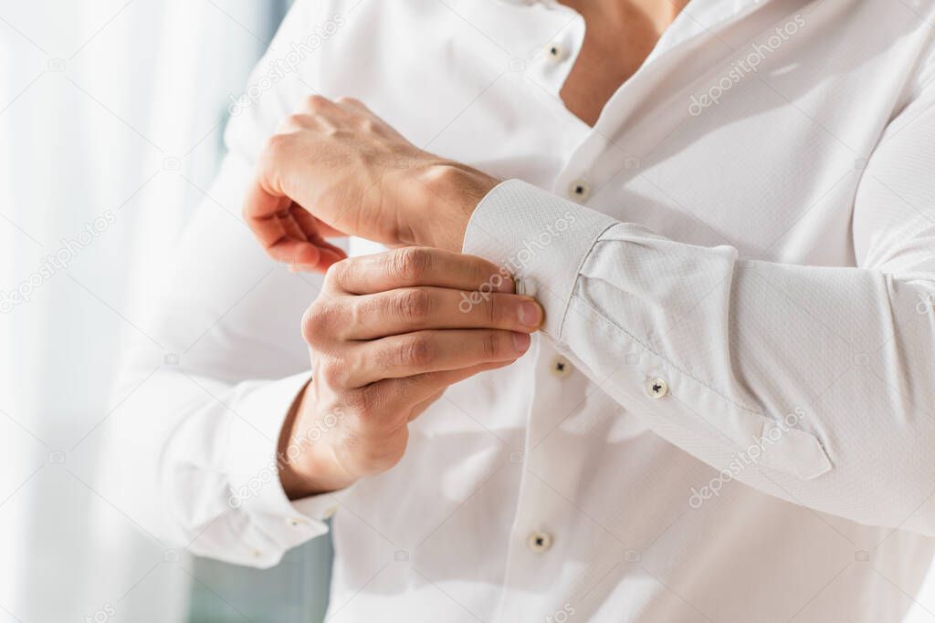 Cropped view of man buttoning cuff of white shirt 