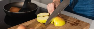 Cropped view of woman cutting apple near eggs and frying pan, banner  clipart