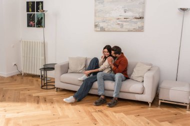 Kanepede gülümseyen sevgiliyi kucaklayan adam 