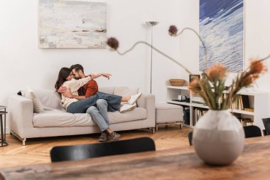 Oturma odasındaki kanepede gülümseyen sevgiliyi kucaklayan adamın yan görüntüsü. 