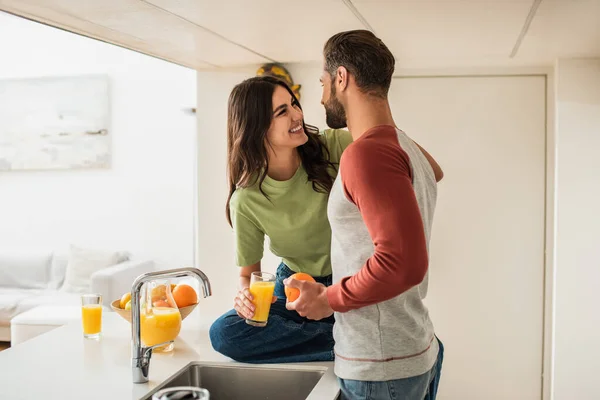 Sorrindo Mulher Olhando Para Namorado Com Laranja Perto Suco Cozinha — Fotografia de Stock