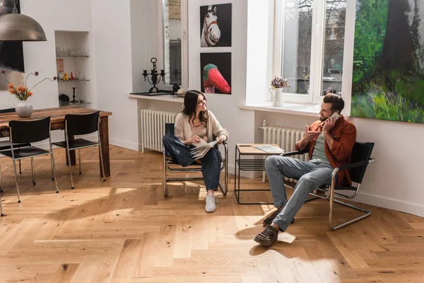 Akıllı telefonu işaret eden bir adam, kız arkadaşının yanında kitapla konuşuyor. 