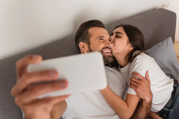 Woman Kissing Boyfriend Selfie Blurred Smartphone Bed — Stock Photo, Image