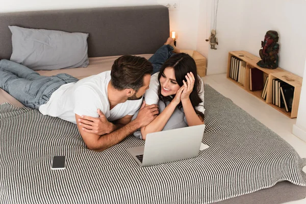 Casal Alegre Olhando Uns Para Outros Perto Dispositivos Cama — Fotografia de Stock