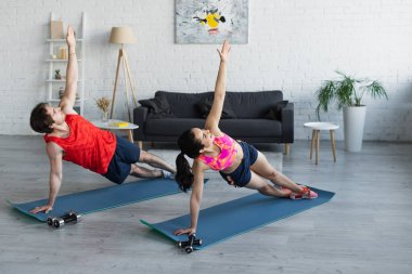 Spor kıyafetli genç bir çift evde spor paspasları üzerinde egzersiz yapıyor.