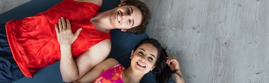top view of young couple in sportswear lying on fitness mats and looking at camera at home, banner clipart