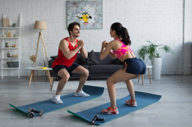 Spor giyim sektöründe genç bir çift modern çatı katındaki spor paspaslarına çömeliyor.