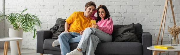 Positive Young Couple Sitting Couch Looking Cellphone Living Room Banner — Stock Photo, Image