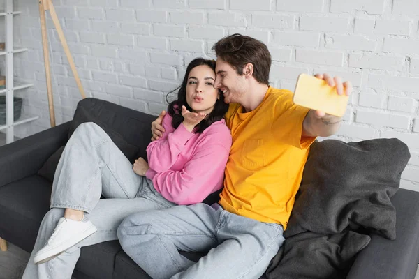 Smiling Young Couple Sitting Couch Taking Selfie Blowing Kiss Gesture — Stock Photo, Image