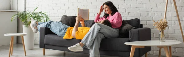 Sonriente Joven Sentada Sofá Con Novio Mintiendo Leyendo Libro Sala — Foto de Stock