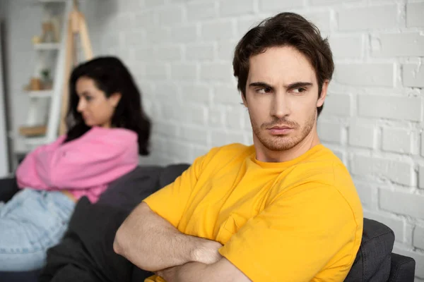 Disappointed Young Man Crossed Arms Sitting Couch Blurred Girlfriend Home — Stock Photo, Image