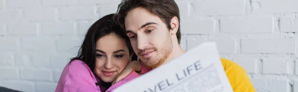 Sonriente Joven Pareja Sentada Sofá Abrazando Leyendo Periódico Casa Pancarta —  Fotos de Stock