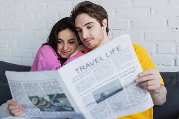 Sonriente Joven Pareja Sentada Sofá Abrazando Leyendo Periódico Casa —  Fotos de Stock