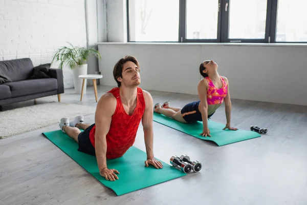 身穿运动服的年轻夫妇在家里的健身垫上摆出瑜伽姿势 — 图库照片