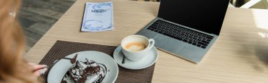 Boş ekranlı dizüstü bilgisayar görüntüsü, kahve ve menü Kafe 'de bulanık ön planda tatlılı kadın, pankart 