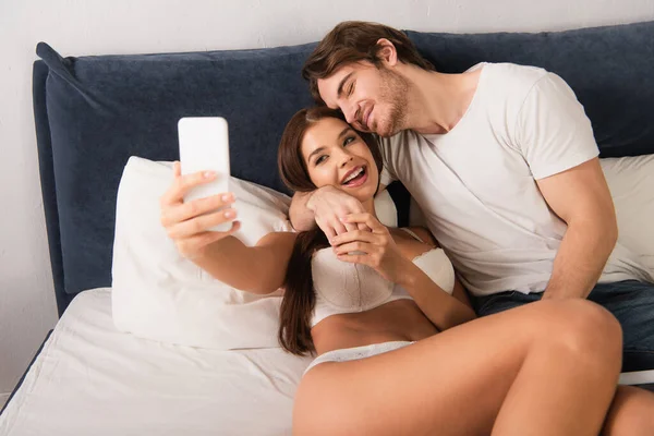 Homem Alegre Namorada Lingerie Tomando Selfie Celular Quarto — Fotografia de Stock