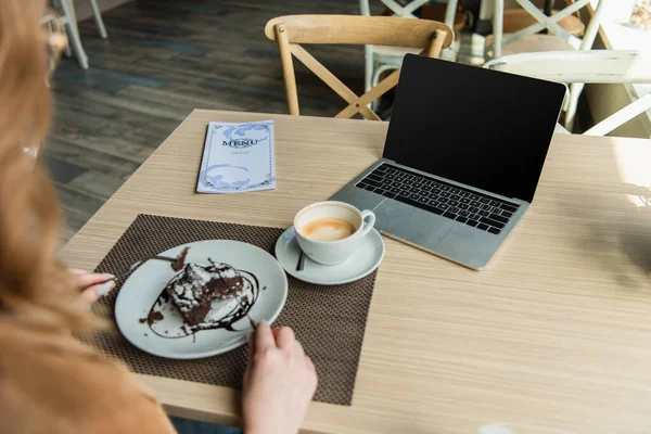 カフェでデザートとぼやけた女性の近くのノートパソコンとコーヒー — ストック写真