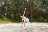 plná délka šťastný mladý žena dělá výpad twist na jóga podložka v lese 