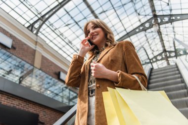 Alışveriş merkezinde cep telefonuyla konuşan gülümseyen bir kadının düşük açılı görüntüsü. 