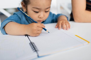 Bulanık Asyalı küçük kız renkli kalemle çiziyor 
