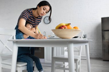 Asyalı kadın kızını çiziyor ve meyvelerini bulanıklaştırıyor 