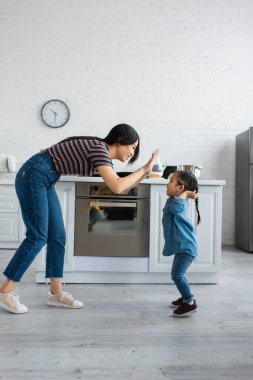 Asyalı anne ve küçük kızının mutfakta beşlik çakışının yan görüntüsü 