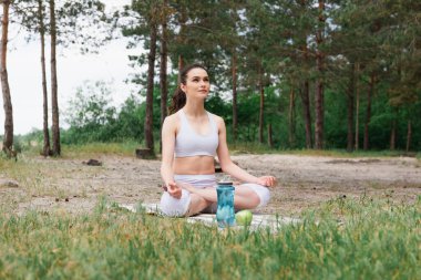 Spor kıyafetli genç bir kadın lotus poz verip yoga minderinde meditasyon yapıyor. 