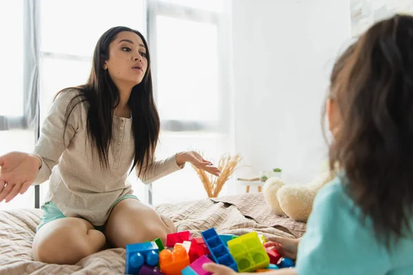 Aziatische Moeder Wijzend Met Handen Buurt Van Kind Bouwstenen Bed — Stockfoto