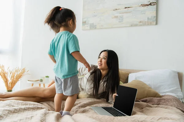 Lächelnde Frau Schaut Tochter Neben Laptop Auf Bett — Stockfoto